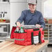 A woman in a chef hat using a red ServIt insulated bag to put trays and bottles in.