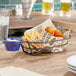 A Clipper Mill black iron oval basket with fried food and a drink in a glass on a table.