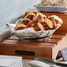 A Clipper Mill stainless steel oval basket with pretzels on a wood cutting board.