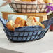 A black iron powder coated oval grid basket filled with bread on a table.