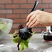 A hand holding a black Choice plastic serving fork over a salad