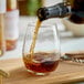 A 12 oz. stemless wine glass being filled with a dark beverage.