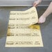 A person using a Rubbermaid yellow spill absorbent pad to cover a spill on the floor.