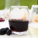 An Acopa stemless wine glass filled with red wine on a table next to blackberries.