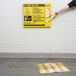 A person's arm and hand putting a yellow Rubbermaid sign on a white brick wall.