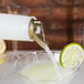 A person using a Carlisle Store 'N Pour container to pour liquid into a glass with a lime wedge.