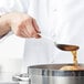 A hand using a Vollrath solid stainless steel basting spoon to pour liquid into a pot.