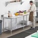 A man in a brown apron standing at a Regency stainless steel work table with undershelf in a kitchen.