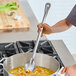 A person using a Vollrath stainless steel basting spoon to stir soup in a pot.