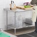 A person standing in front of a Regency stainless steel work table with undershelf.