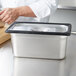 A person using a Vollrath black silicone band to cut food in a stainless steel container on a counter.