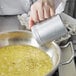 A hand using a Vollrath aluminum shaker to pour a liquid into a pot.