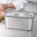 A person using a Vollrath gray silicone band to prepare food in a stainless steel steam table pan.