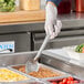 A hand using a Vollrath perforated basting spoon to serve food from a tray.