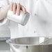 A chef using a Vollrath aluminum shaker to pour salt into a bowl.