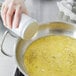 A hand holding a Vollrath Coarse Aluminum Shaker over a pan of food.