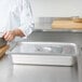 A chef's hand using a gray silicone band to prepare food in a large stainless steel pan.