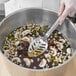 A person using a Vollrath slotted basting spoon to stir soup in a pot.