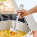 A person holding a Vollrath stainless steel perforated basting spoon over a pot of food.