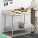 A man cutting vegetables on a Regency stainless steel work table with undershelf.