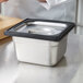 A person using a Vollrath black silicone band to prepare food in a stainless steel container.