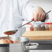 A chef using a Vollrath stainless steel basting spoon to stir liquid in a pot.