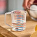 A person using a clear Rubbermaid Bouncer measuring cup to measure liquid ingredients.