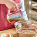 A person pouring oil into a bowl using a Rubbermaid clear polycarbonate measuring cup.