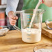 A person pouring milk into a Rubbermaid clear plastic measuring cup.