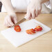 A person cutting strawberries on a white Choice cutting board.