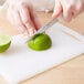 A person slicing a lime on a Choice white bar size cutting board with a knife.