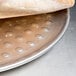 A person holding a piece of bread on an American Metalcraft aluminum pizza pan with nibs.