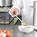 A chef using a Vollrath hooked handle solid spoon to prepare food in a bowl.