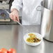 A chef using a Vollrath hooked handle solid spoon to stir a bowl of food.
