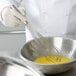 A person using a Vollrath stainless steel piano whisk to mix eggs in a silver bowl.