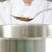 A person using a Vollrath hooked slotted spoon to pour food into a large pot on a counter.