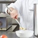 A chef using a Vollrath hooked slotted spoon to stir food in a bowl.