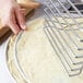 A person using an American Metalcraft pizza pan rack to hold pizza dough.