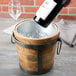 A bottle of wine being poured into a wooden bucket of ice.