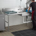 A man washing dishes on a Regency soiled dish table in a commercial kitchen.