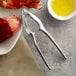 A lobster claw with a Choice zinc-plated steel lobster cracker next to a plate of food.