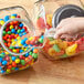 A hand using a Choice clear plastic utility scoop to pour yellow candy into a jar.