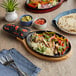 A Choice oval cast iron fajita skillet with chicken, vegetables and tortillas on a table.