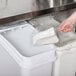 A hand using a Baker's Mark clear plastic utility scoop to scoop white powder into a container.