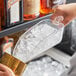 A hand using a Choice clear plastic utility scoop to pour ice into a glass.