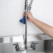 A person using a T&S pre-rinse faucet over a sink.