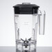 A clear Waring blender jar with black handles and lid.