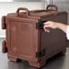 A hand opening a dark brown Cambro food pan carrier on a counter.