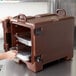 A woman using a Cambro dark brown front-loading insulated food pan carrier with food trays inside.