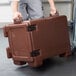 A man wheeling a brown Cambro Ultra Pan Carrier with a pocket on the back.